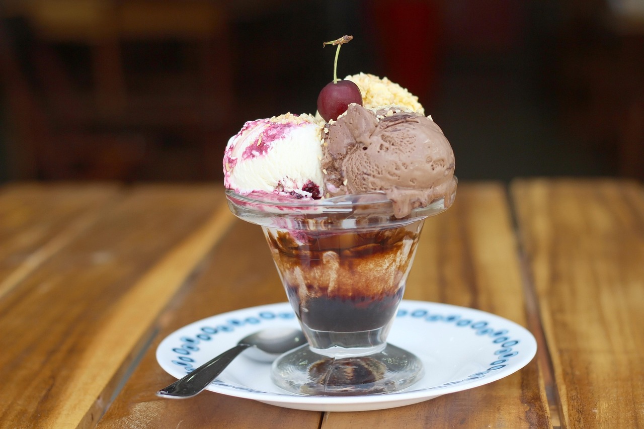 Scoops of vanilla and chocolate ice cream topped with a cherry in a glass dessert cup
